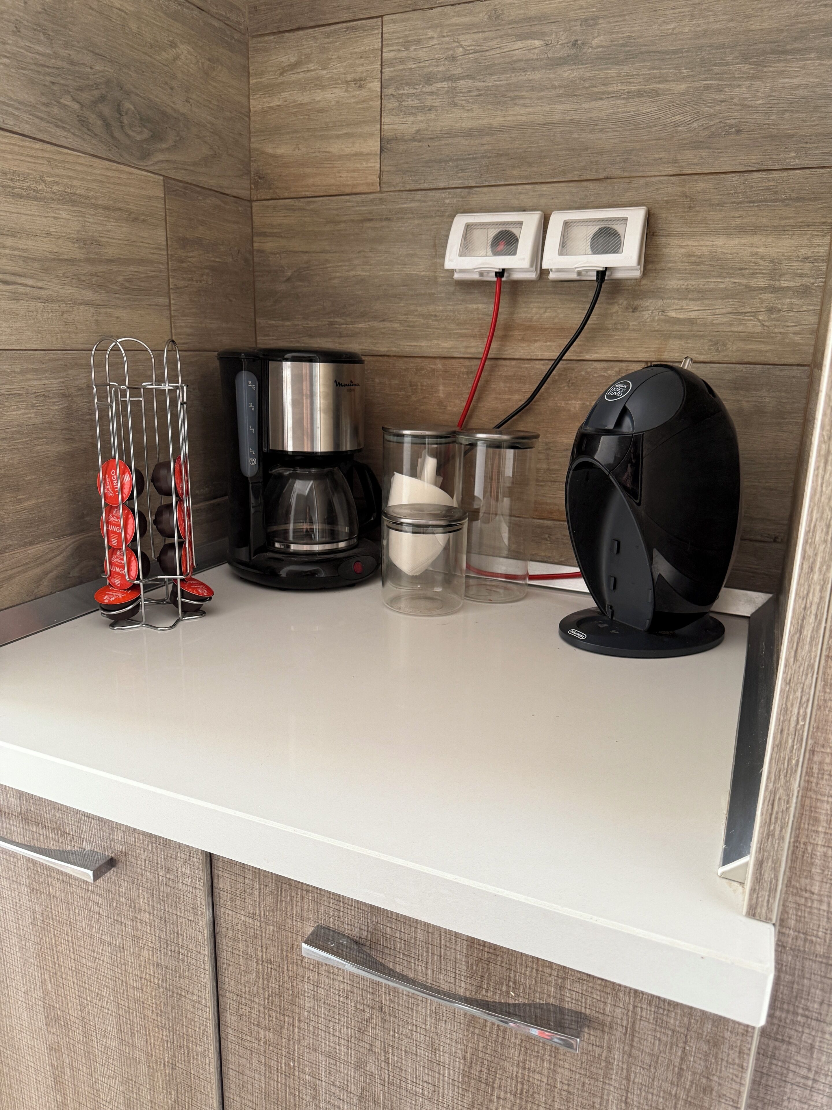 Une petite cuisine équipée d’une machine à café, d’un ventilateur et d’un support pour capsules de café.