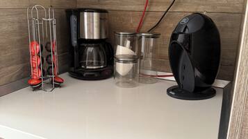 Une petite cuisine équipée d’une machine à café, d’un ventilateur et d’un support pour capsules de café.