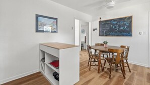 A dining area with a wooden table and chairs, a chalkboard with writing, and a framed picture on the wall. - Shem Shack-Old Village, 5 mins to Beach (Mount Pleasant)