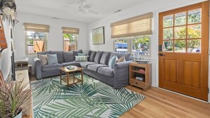 A living room with a grey sectional sofa, a coffee table, a wooden side table, and a large window with a view of the outdoors. - Shem Shack-Old Village, 5 mins to Beach (Mount Pleasant)