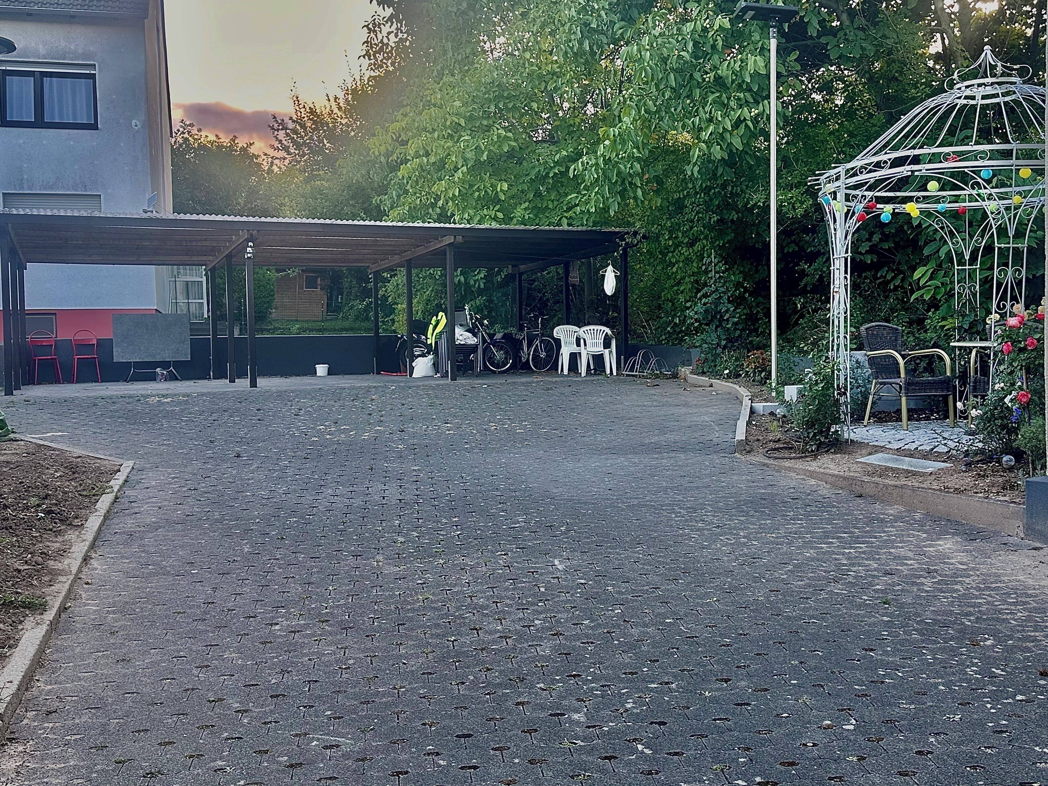 A covered outdoor area with a paved walkway, a sheltered seating area with chairs, and a decorative metal structure with colorful balls.