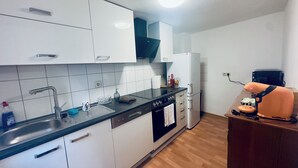 A modern kitchen with white cabinets, a black countertop, a built-in oven, and a white refrigerator. - 2-room apartment in the center of Friedrichsdorf (Friedrichsdorf)