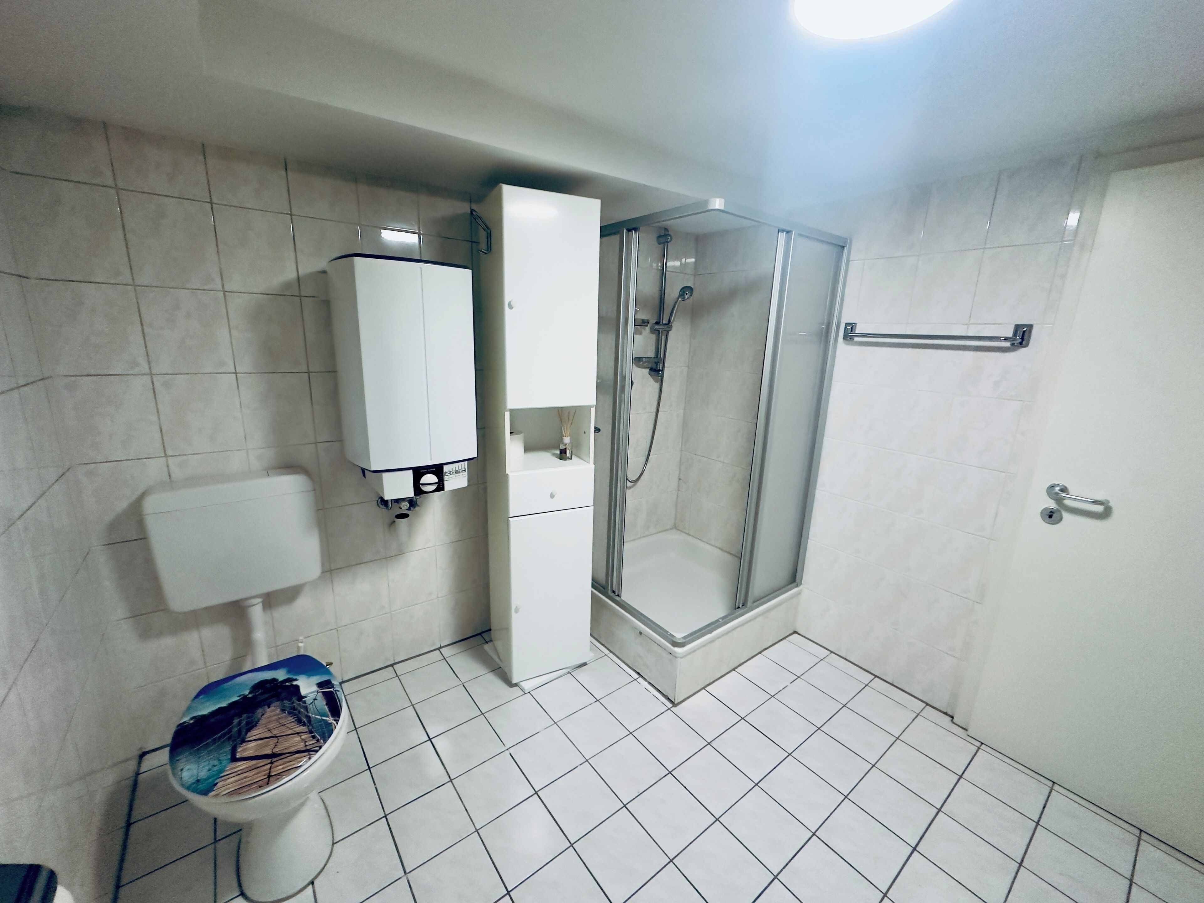 Un baño con inodoro, ducha y un armario blanco.