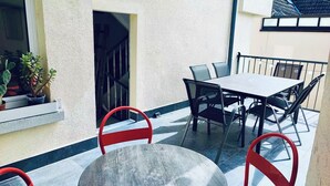 A patio with a round table and four chairs, a window with potted plants, and a view of a building in the background. - 2-room apartment in the center of Friedrichsdorf (Friedrichsdorf)