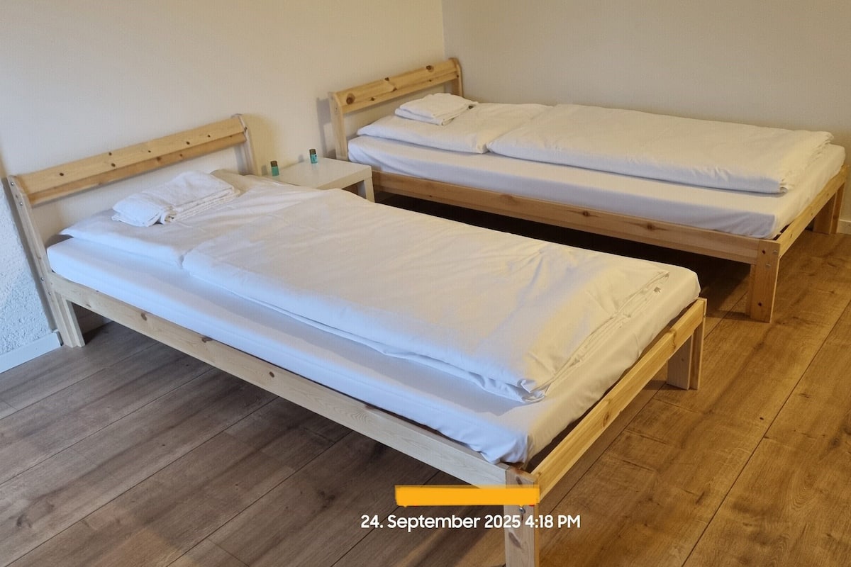 Two wooden single beds with white linens in a room with wooden flooring.