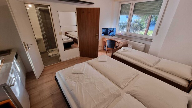 A room with two beds, a desk, a TV, and a window with blinds. - Hotel 3H Mannheim (Mannheim)