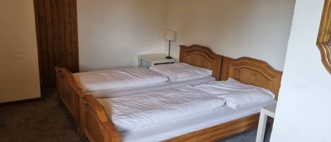 Habitación individual con una cama de una sola plaza, cabecera de madera, una mesita de noche con lámpara y piso cubierto de alfombra.