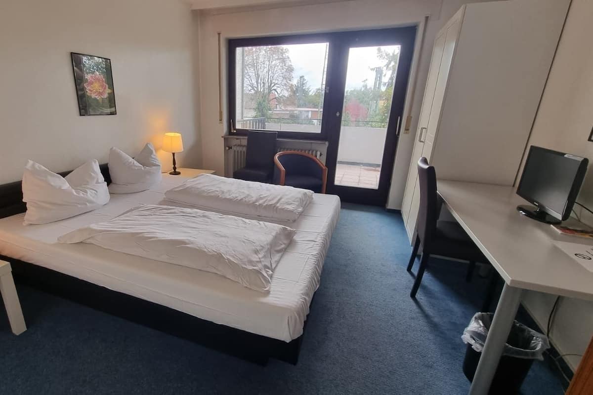 A hotel room with a bed, a desk, a chair, a lamp, and a window.