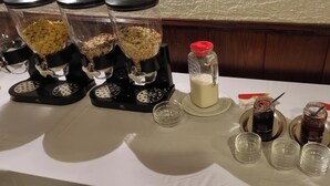A table with coffee machines, a milk dispenser, and various condiments. - Hotel 3H Mannheim (Mannheim)