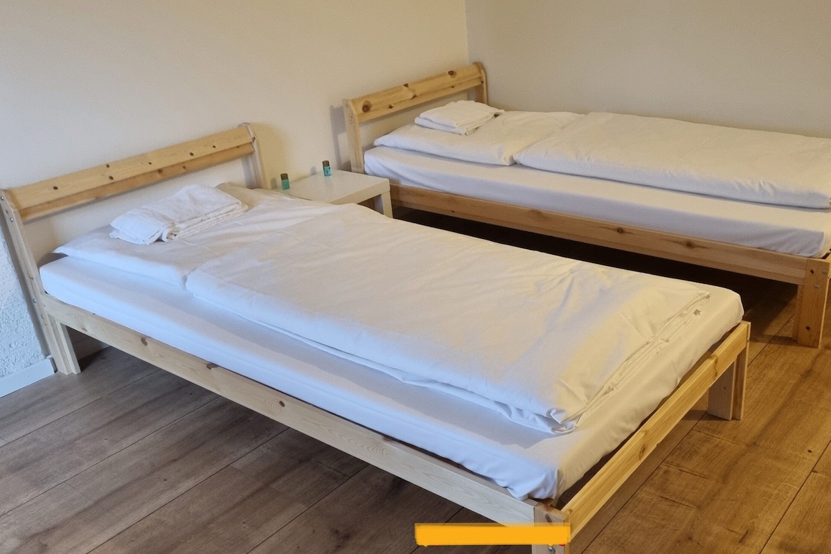 Zwei hölzerne Einzelbetten mit weißen Laken in einem Zimmer mit Holzboden.