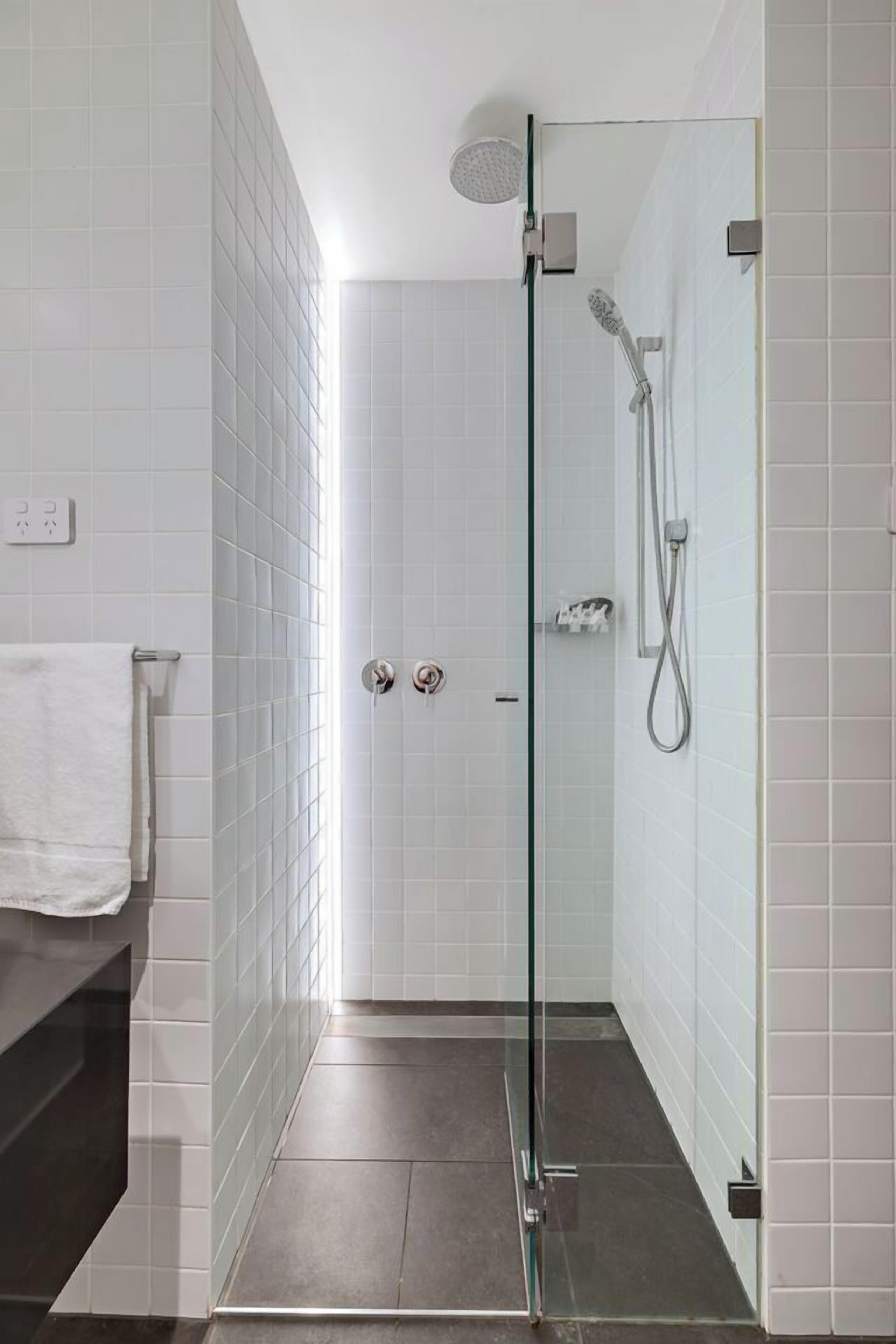 A modern bathroom with white tiled walls, a glass shower enclosure, and a dark floor.