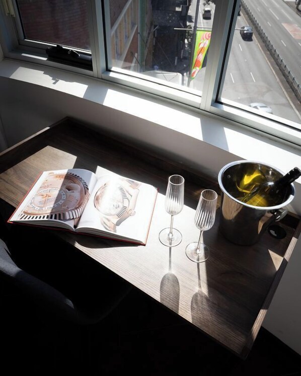A table by a window with a book, wine glasses, and a bottle of wine.