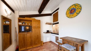 Une petite cuisine avec des meubles de rangement en bois, un téléviseur et une table en bois accompagnée d’un banc.