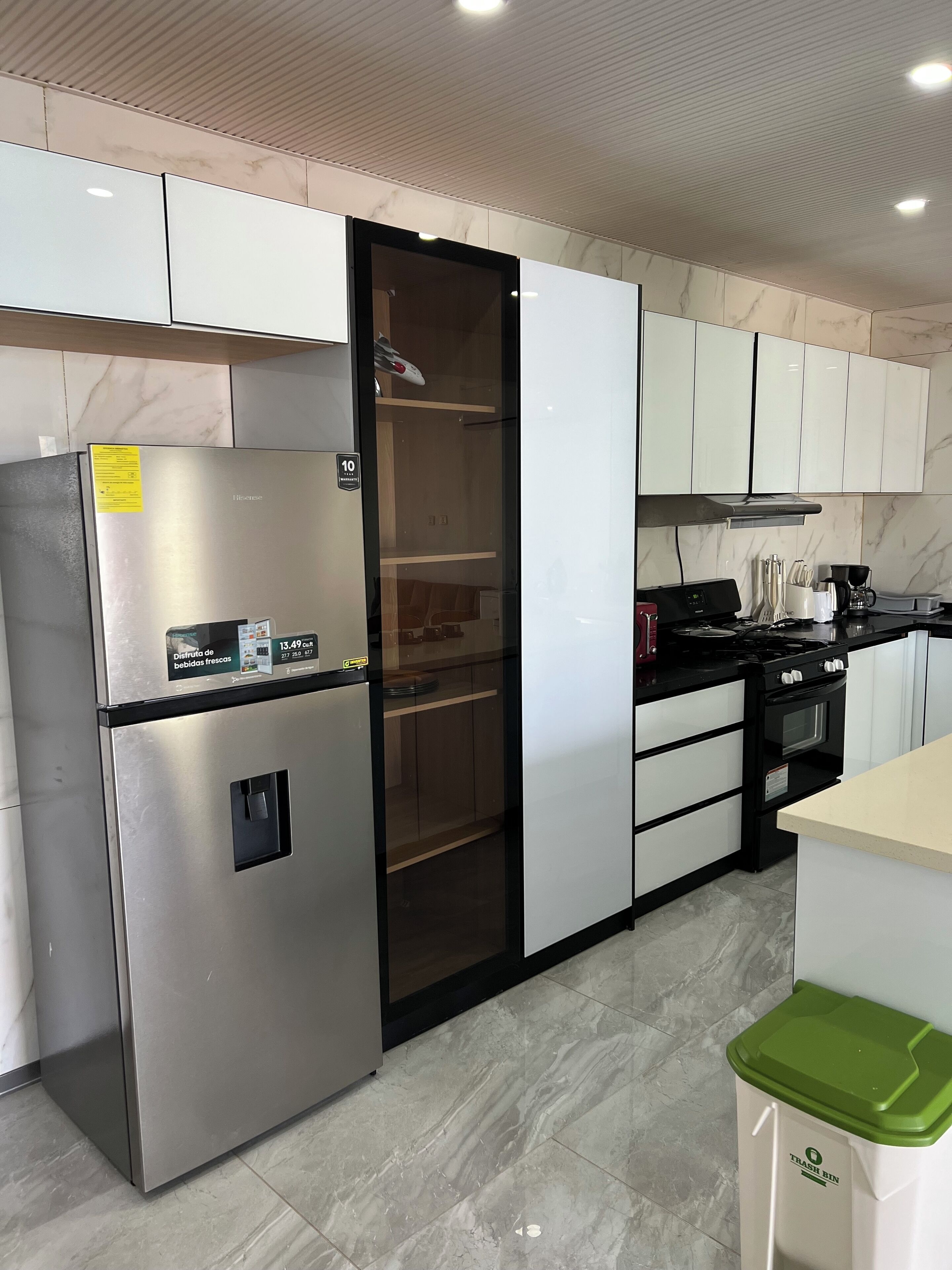 Una cocina con un refrigerador de acero inoxidable, un microondas, una estufa y un cesto de basura.