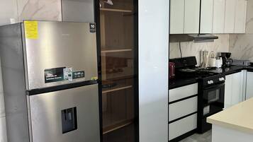 Una cocina con un refrigerador de acero inoxidable, un microondas, una estufa y un cesto de basura.
