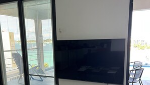 A modern living room with a large flat-screen TV, a sliding glass door leading to a balcony with a pool, and a tiled floor. - Beach Front 2 Bed Condon C1.1 with Sea View and Private Pool !! (Simpson Bay)