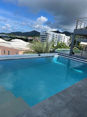 A rooftop pool with clear blue water, surrounded by buildings and mountains in the background.