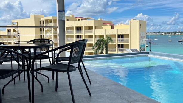 A poolside area with outdoor seating and a view of a hotel building and the sea. - Beach Front 2 Bed Condon C1.1 with Sea View and Private Pool !! (Simpson Bay)