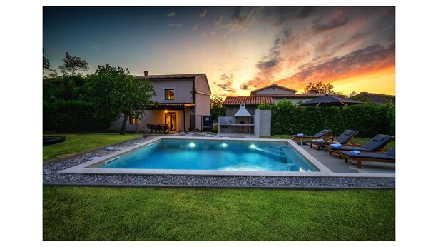 Une piscine avec des chaises longues, un espace barbecue et une maison dotée d’une terrasse.