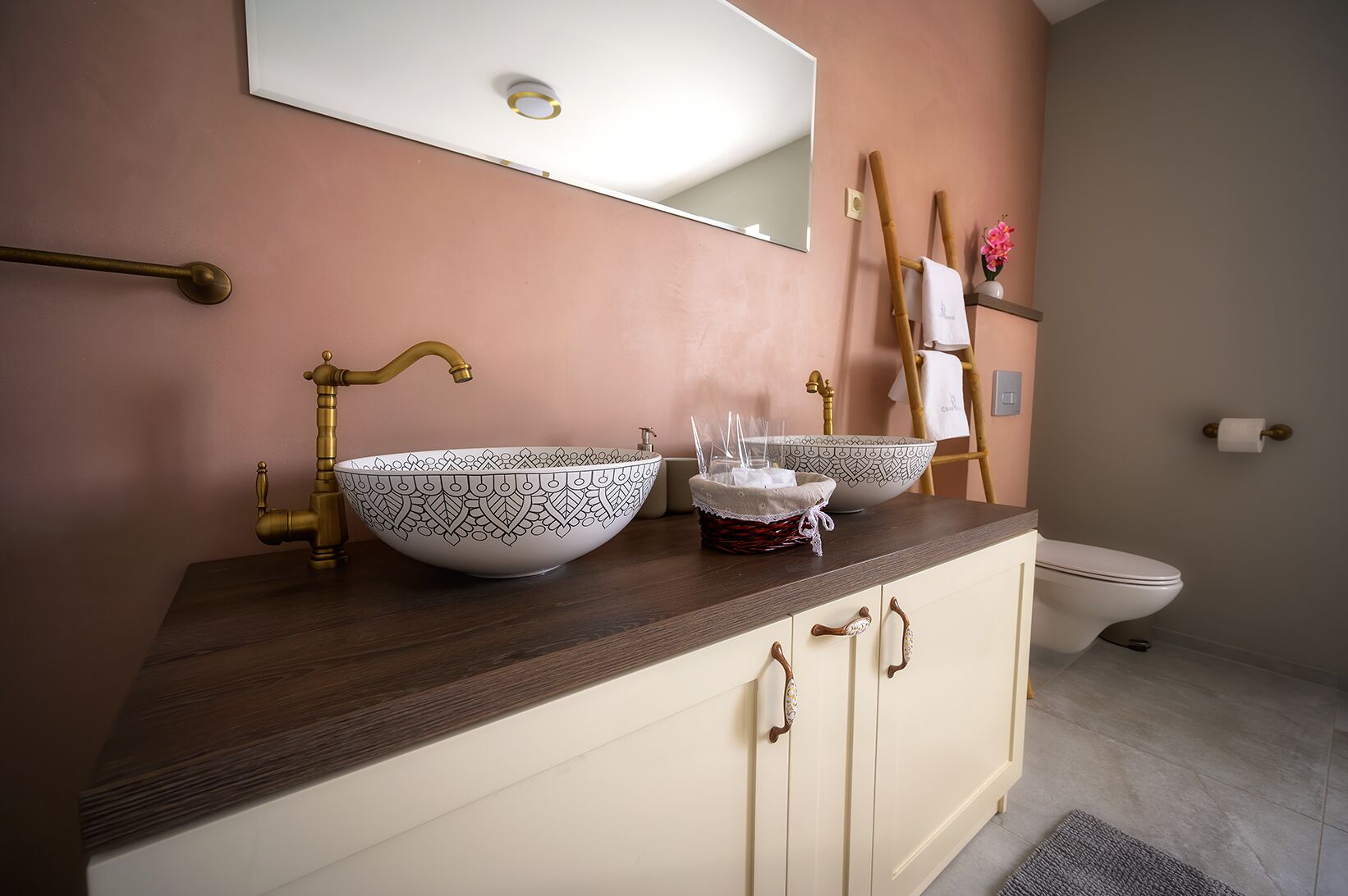 Une salle de bain avec deux grands lavabos blancs ornés de motifs noirs, un meuble-lavabo en bois, un miroir, un porte-serviettes et des toilettes.