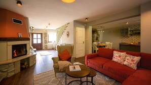 Un salon chaleureux avec une cheminée, un canapé rouge et, au fond, un coin repas.