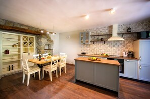 Une cuisine compacte avec un coin repas, agrémentée d’un mur en pierre, d’un pare-feu en carrelage et d’un plancher en bois.
