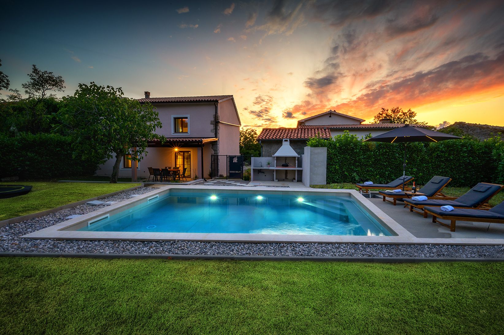 A swimming pool with lounge chairs, a barbecue area, and a house with a patio.