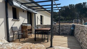 Eine Terrasse mit Tisch, Stühlen, einem Grill und einer Steinmauer.