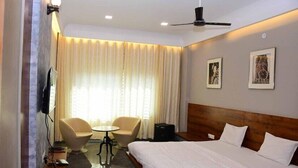 A hotel room with a bed, a desk, two chairs, a television, and a ceiling fan. - HOTEL SY21 (Dhar)