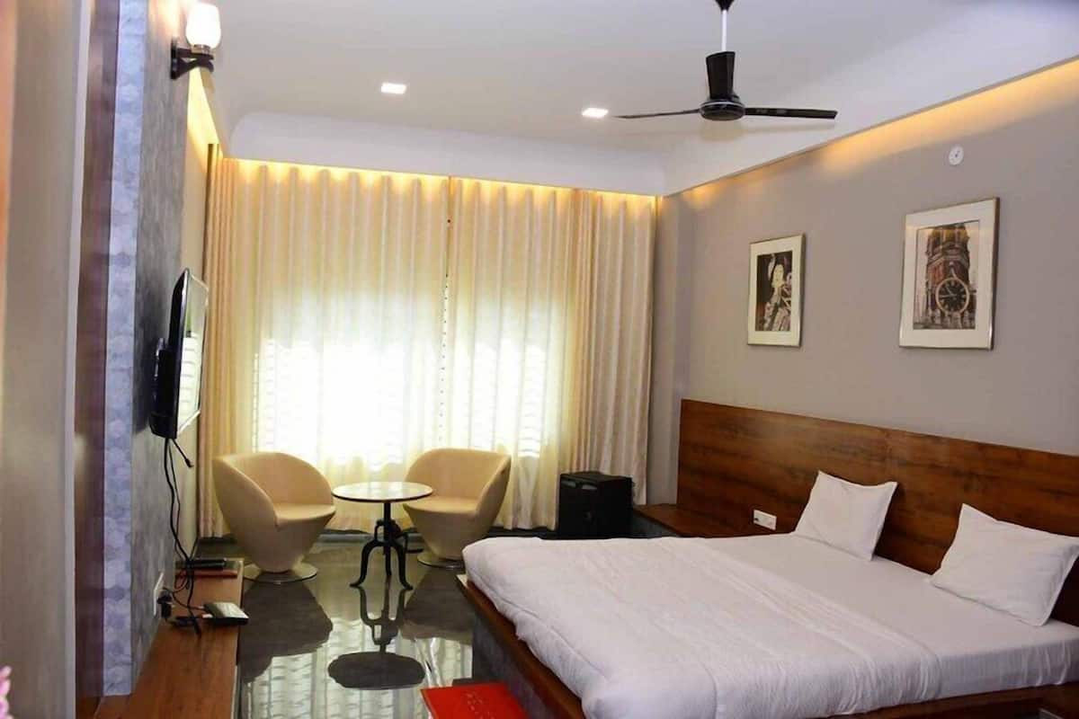 A hotel room with a bed, a desk, two chairs, a television, and a ceiling fan.