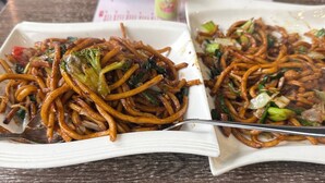 Two plates of stir-fried noodles with vegetables on a wooden table. - The Sheger Addis Blue Luxury Hotel (Addis Ababa)