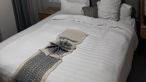 A neatly made bed with white linens and a decorative throw. There is a headboard, a nightstand, and a wall-mounted lamp. - The Sheger Addis Blue Luxury Hotel (Addis Ababa)