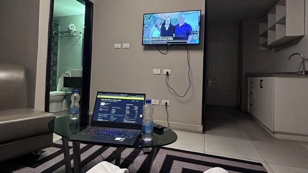 A hotel room with a TV mounted on the wall, a laptop on a glass table, a water bottle, and a bed with a striped rug. - The Sheger Addis Blue Luxury Hotel (Addis Ababa)