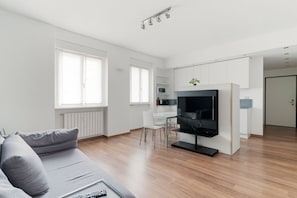 Un saló modern amb un sofà gris, un televisor de pantalla plana i zona menjador amb taula i cadires blanques.