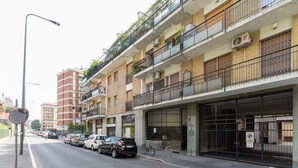 Un immeuble à plusieurs étages doté de balcons, dont la devanture est bien visible, et où des voitures sont garées le long de la rue.