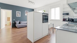 Une cuisine moderne avec des armoires blanches, un four encastré et un coin repas comprenant une table et des chaises blanches.