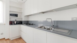 Une cuisine moderne avec des meubles blancs, un évier en acier inoxydable, un four à micro-ondes et une cuisinière à gaz.