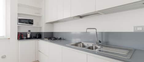 Une cuisine moderne avec des meubles blancs, un évier en acier inoxydable, un four à micro-ondes et une cuisinière à gaz.