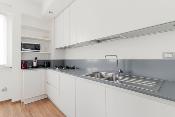Una cocina moderna con armarios blancos, un lavamanos de acero inoxidable, un microondas y una estufa a gas.