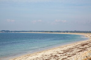 A coastal beach with clear water, sandy shore, and distant buildings. - Apartment 'Appartement Drenec' with Shared Garden and Wi-Fi (Fouesnant)