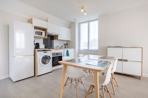 Une cuisine moderne avec un coin repas, comprenant un four à micro-ondes, un four, un lave-linge et une table avec des chaises.