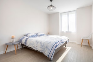 Une chambre à coucher avec un lit, une table de chevet, une lampe, une chaise et une fenêtre.