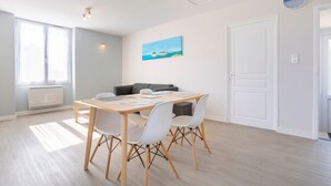 A modern room with a wooden dining table, white chairs, a gray sofa, and a painting of a beach scene.