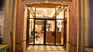 Ein Hotel Eingangsbereich mit Schachbrettboden, einer Rezeption und einer Person, die auf einer Bank sitzt.