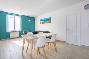 Una stanza con un tavolo da pranzo, sedie, un divano, una finestra con tende, un termosifone, un quadro e una porta.