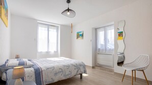 A bedroom with a bed, bedside table, lamp, chair, and a large mirror on the wall. - Apartment 'Penfret' with Private Terrace, Shared Garden and Wi-Fi (Fouesnant)
