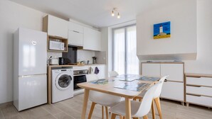 A modern kitchen with a refrigerator, microwave, washing machine, and wooden cabinets. - Apartment 'Penfret' with Private Terrace, Shared Garden and Wi-Fi (Fouesnant)