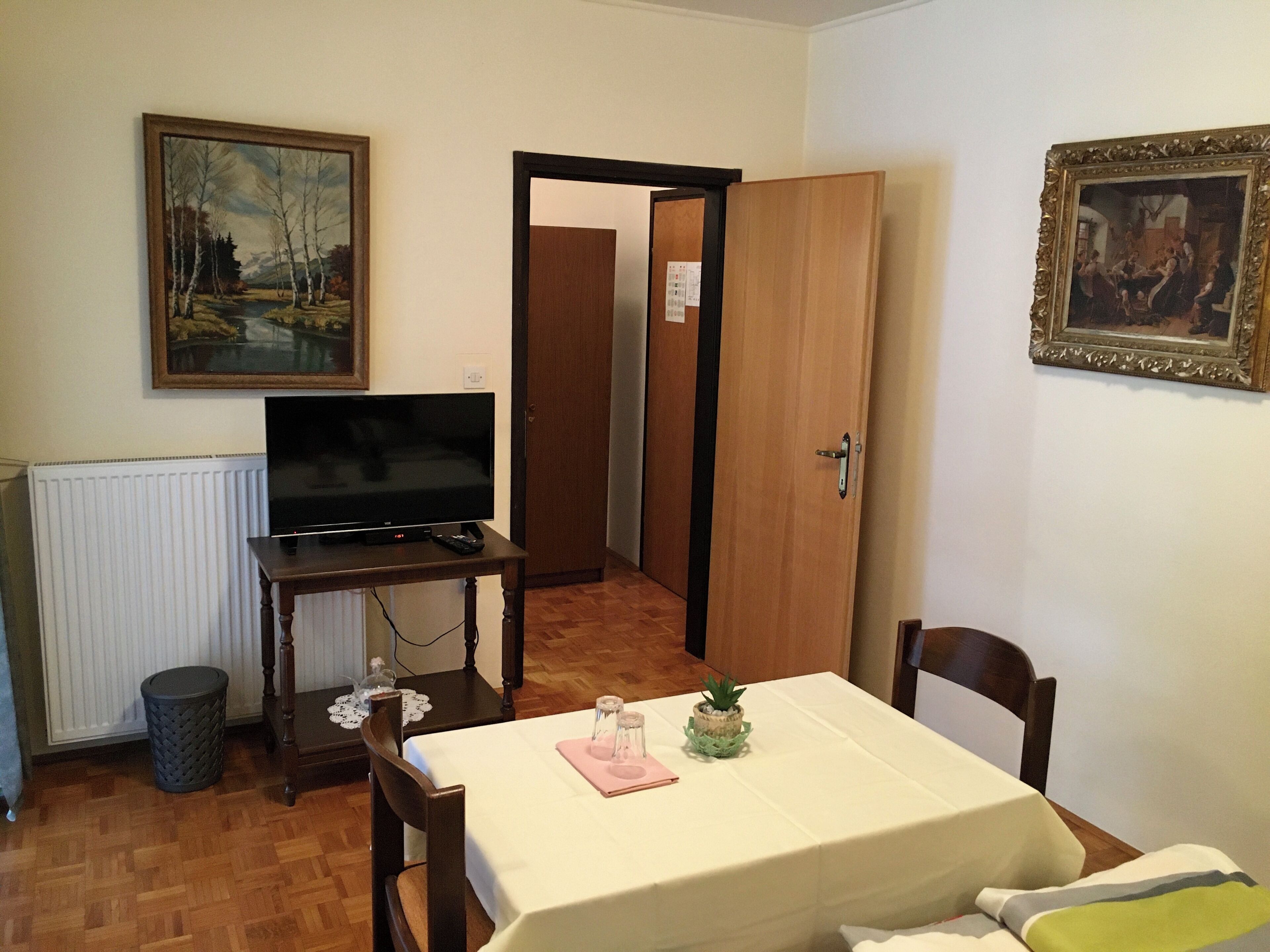 Una habitación con una televisión sobre una mesa de madera, un cuadro en la pared y una puerta que da a otra estancia.