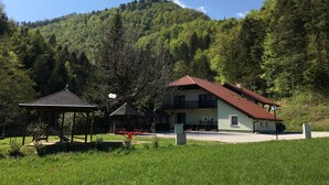 A building with a red roof, a covered outdoor area with a swing set, and a forested hillside in the background. - Gostišče Atelšek (Rečica ob Savinji)
