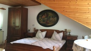A bedroom with a wooden ceiling, a large bed with a headboard, a nightstand, a dresser, and a painting on the wall. - Gostišče Atelšek (Rečica ob Savinji)